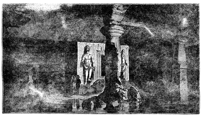 A view of a cave, with large statues and pillars and two people standing inside.